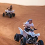 Tourist riding a quad bike aggressively on a desert sand dune in Dubai during a Trawey Tours safari.