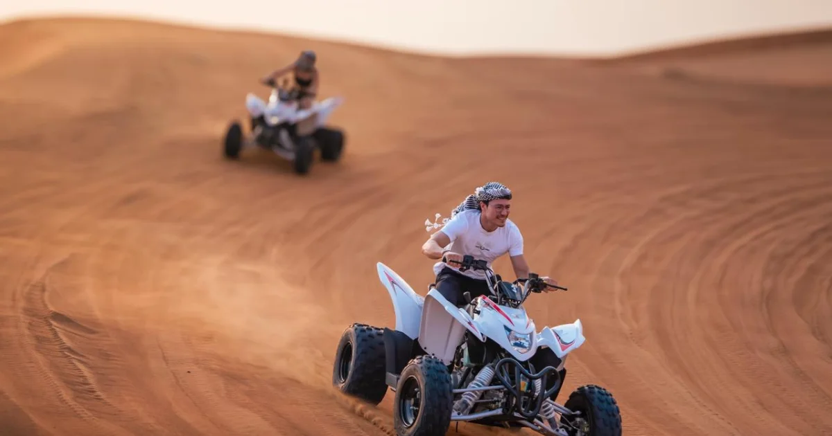Tourist riding a quad bike aggressively on a desert sand dune in Dubai during a Trawey Tours safari.