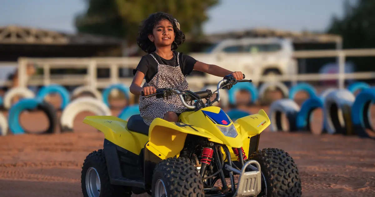 Young girl riding a safe mini quad bike for kids in the Dubai desert on a secure track.