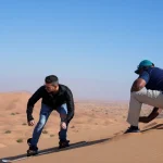 Beginner practicing the sideways sandboarding stance with a Trawey Tours guide on a Dubai dune.