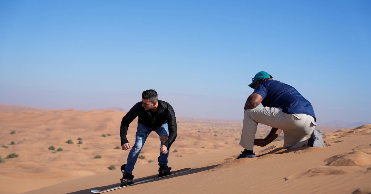 Two men wearing sneakers and outdoor gear walking on sand dunes during a Dubai desert safari.