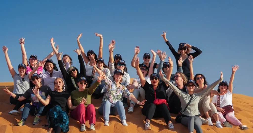 Corporate team posing for a group photo on a golden dune during a desert safari team-building event.