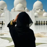 Woman in a black abaya admiring the white marble domes of Sheikh Zayed Grand Mosque in Abu Dhabi.