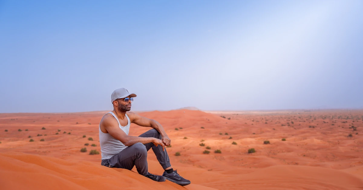 A traveler taking a rest on a red sand dune during a sunny desert safari in Dubai.