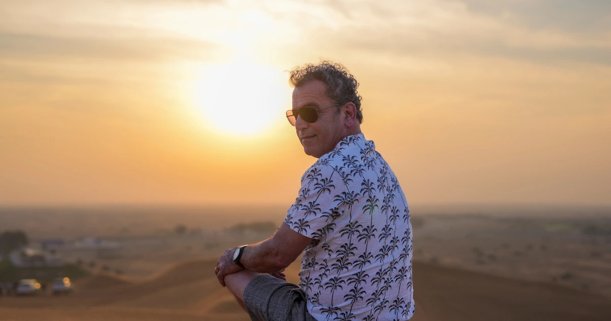 A relaxed senior traveler taking a quiet moment to appreciate a peaceful desert safari sunset.