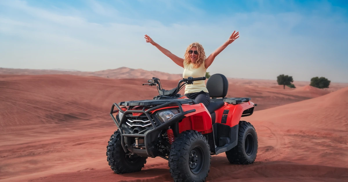 A woman enjoying an adventurous quad bike ride across the red sand dunes during a Dubai desert safari.