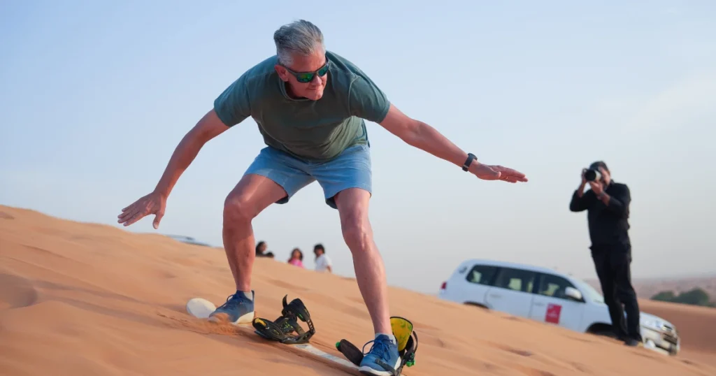 Active senior man enjoying a luxury desert sandboarding tour; adventure travel for retirees and silver surfers.