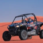 A couple driving a two-seater dune buggy across the red sand dunes during a romantic Dubai desert safari