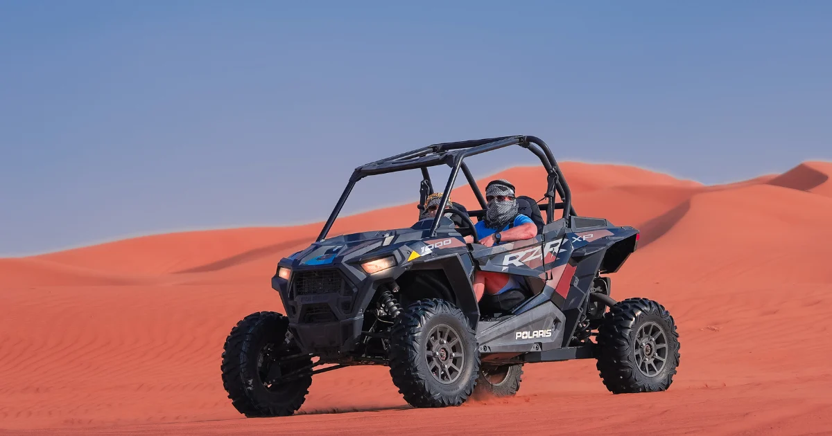 A couple driving a two-seater dune buggy across the red sand dunes during a romantic Dubai desert safari