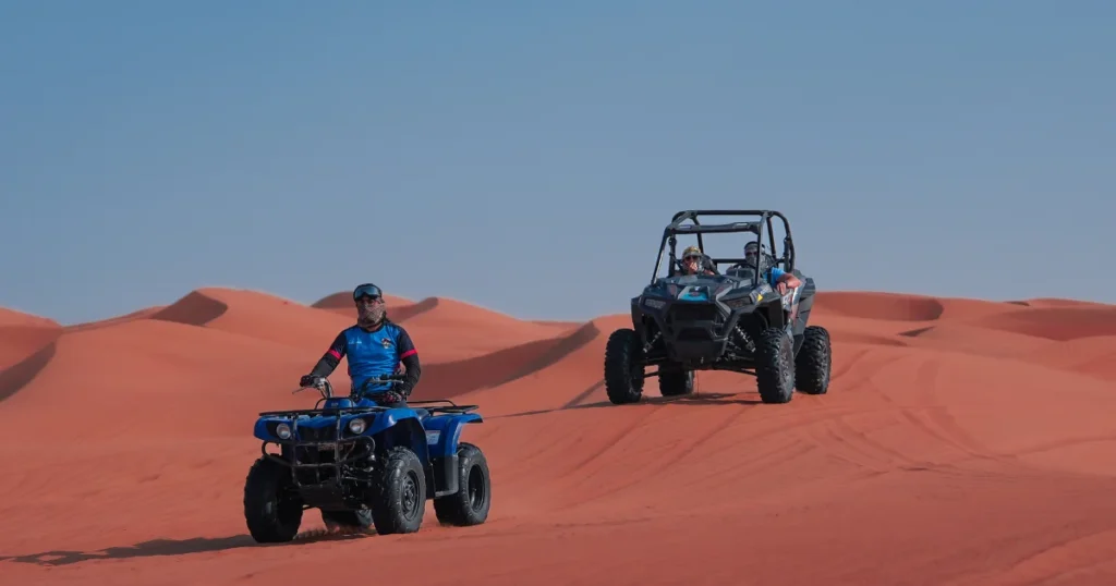 "A guide on a blue quad bike leading a dune buggy across the red sand dunes during a Dubai desert tour."