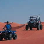 "A guide on a blue quad bike leading a dune buggy across the red sand dunes during a Dubai desert tour."