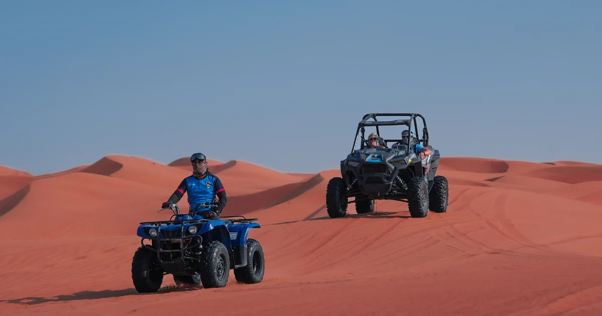 "A guide on a blue quad bike leading a dune buggy across the red sand dunes during a Dubai desert tour."